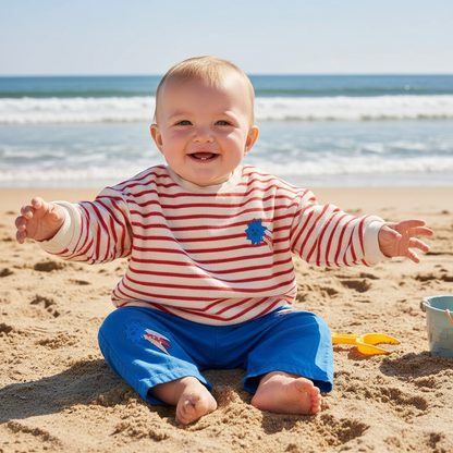 Baby zittend in gestreepte sweater en blauw broekje op strand